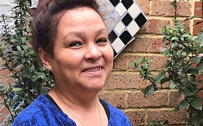 Milly standing in front of a brick wall and a bush