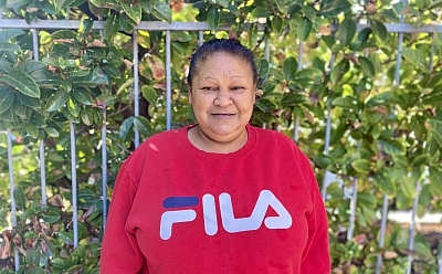 Lynette standing in front of a fence with a large green plant growing behind it