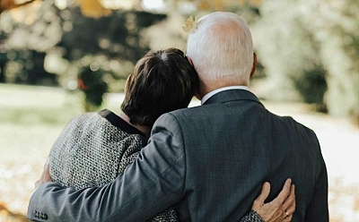 Two smartly dressed people in a park with their arms wrapped around each other.